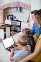 Parents and kids using laptop in kitchen