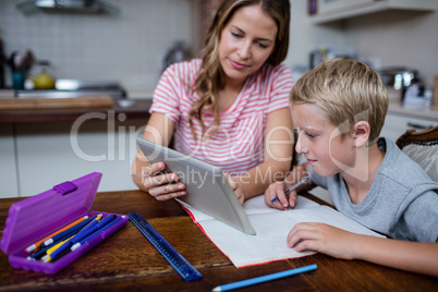 Mother using a digital tablet while helping son with his homewor