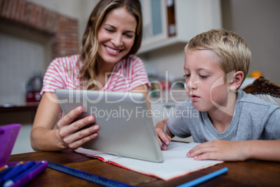 Mother using a digital tablet while helping son with his homewor