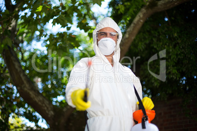 Man spraying insecticide while standing against tree