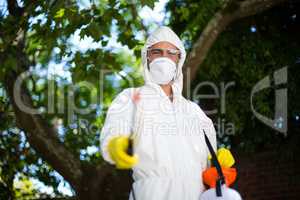 Man spraying insecticide while standing against tree