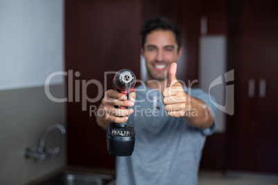 Smiling man showing thumbs up while holding cordless hand drill