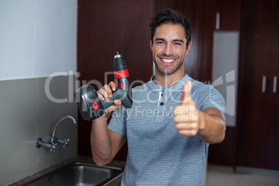 Happy man showing thumbs up while holding cordless hand drill