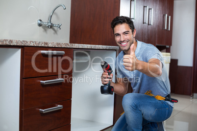 Cheerful man showing thumbs up while using cordless hand drill
