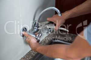 Cropped hands of man fixing faucet with wrench