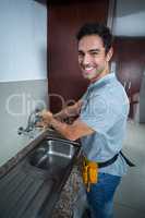 Smiling man fixing faucet with wrench