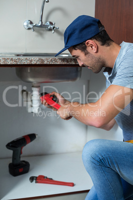 Man using pipe wrench while fixing sink pipe
