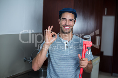 Happy man showing ok sign while holding pipe wrench