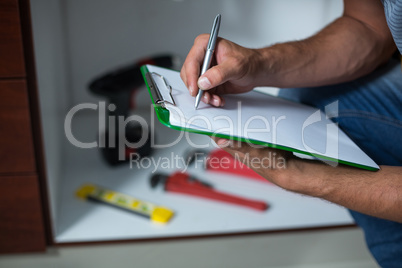 Midsection of man writing on clipboard