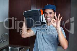 Smiling man carrying toolbox while showing ok sign