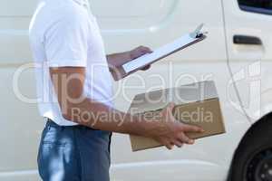 Midsection of delivery man with clipboard and cardboard box