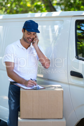 Delivery man writing in clipboard while talking on mobile phone