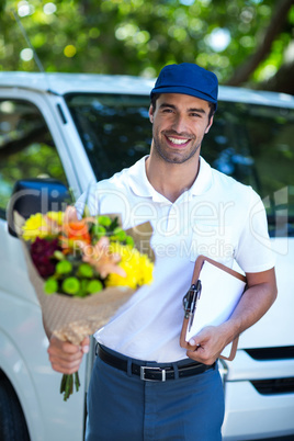 Happy delivery man holding flower bouquet and clipboard