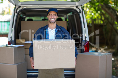 Portrait of smiling delivery man carrying cardboard box