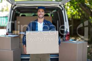 Portrait of smiling delivery man carrying cardboard box