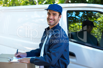 Portrait of happy delivery person writing in clipboard