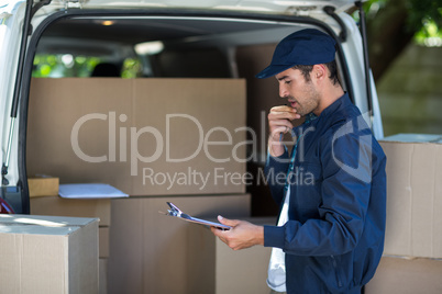 Thoughtful delivery man holding clipboard