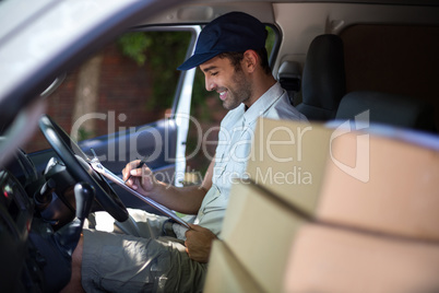 Smiling delivery man writing in clipboard