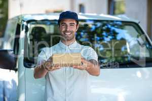 Portrait of cheerful delivery man giving cardboard box