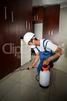 Manual worker spraying insecticide below cabinets