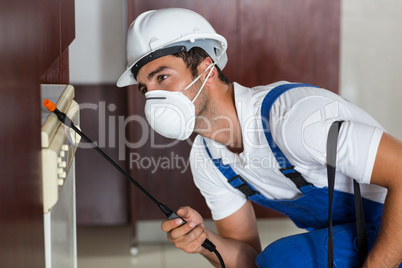 Pest worker using sprayer on cabinets in kitchen