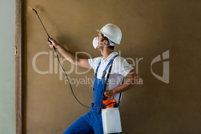 Side view of manual worker spraying chemical on wall