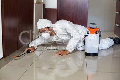 Pest worker using sprayer in kitchen