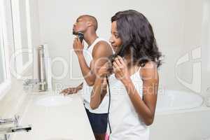 Young man shaving and young woman straightening hair