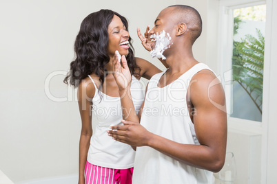 Young woman applying shaving cream on young mans face