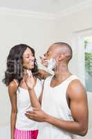 Young woman applying shaving cream on young mans face