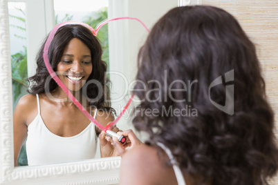 Beautiful young woman drawing big heart on mirror