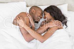 Young couple lying on bed face to face and laughing