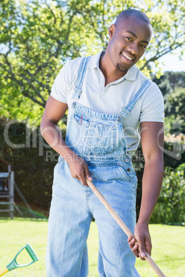 Young man in dungarees raking the garden