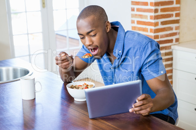 Young man having breakfast and using digital tablet