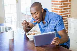 Young man having breakfast and using digital tablet