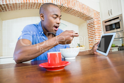 Young man having breakfast and using digital tablet