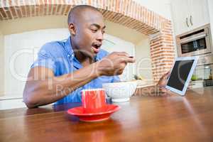 Young man having breakfast and using digital tablet