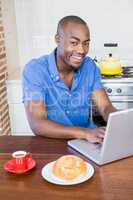 Young man having breakfast and using laptop