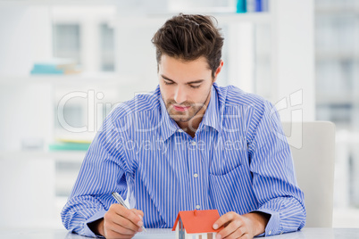 Businessman holding a model house and writing on paper