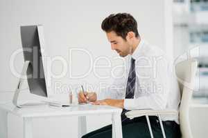 Businessman using computer and taking notes