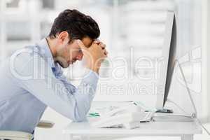 Frustrated businessman sitting on desk with hand on head