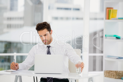 Businessman using laptop and taking notes