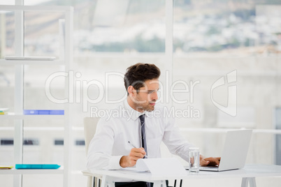 Businessman using laptop and taking notes