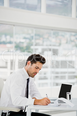 Businessman using laptop and taking notes