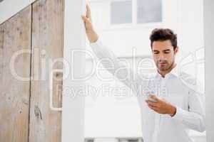 A businessman is looking his smartphone and posing his hand on a