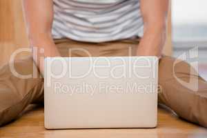 Mid-section of man sitting on the floor and using laptop