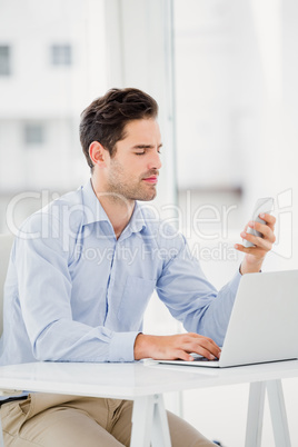 Businessman text messaging on phone while using a laptop