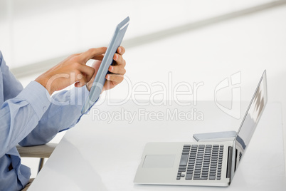 Mid-section of businessman using digital tablet with laptop on t