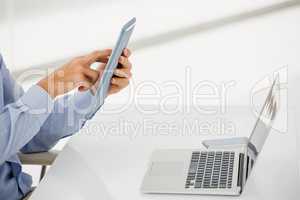 Mid-section of businessman using digital tablet with laptop on t