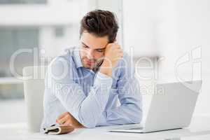 Tensed businessman sitting at table with laptop